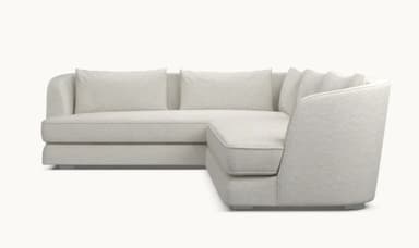 A modern sectional sofa with a light beige fabric upholstery. The sofa features a chaise lounge on the left and a sofa section on the right, with loose back cushions. The design is minimalist with clean lines and a low profile, supported by subtle metallic legs. — 3D model