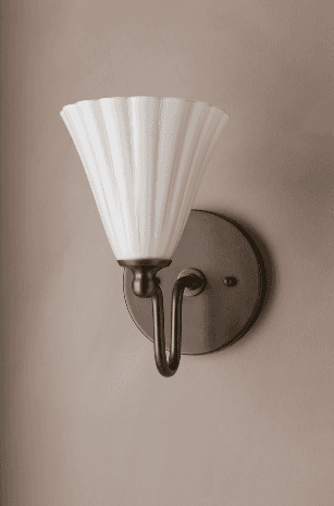 A single wall sconce featuring a conical, fluted shade made of opal glass. The shade is supported by a curved metal arm with a dark bronze or antique brass finish, which extends from a circular wall-mounted backplate of the same material and finish. — 3D model