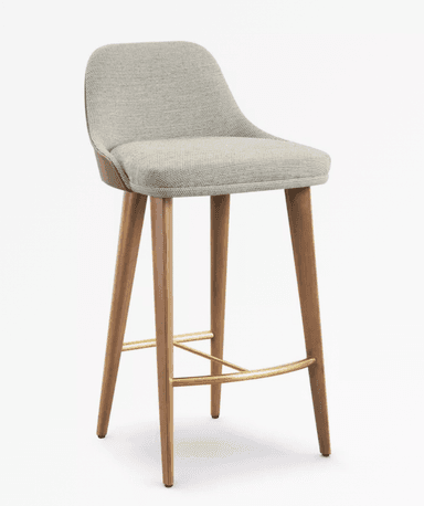 A contemporary bar stool featuring a light grey upholstered seat and low back, supported by four tapered wooden legs with polished brass footrests. — 3D model
