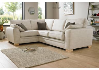 An L-shaped sectional sofa upholstered in a light beige or cream fabric. The sofa features a modern, clean-lined design with wide armrests and low-profile wooden block feet. It is composed of multiple individual seating modules that form a corner configuration. The seating area includes several seat cushions, backrest cushions, and two dark gray rectangular accent pillows. — 3D model
