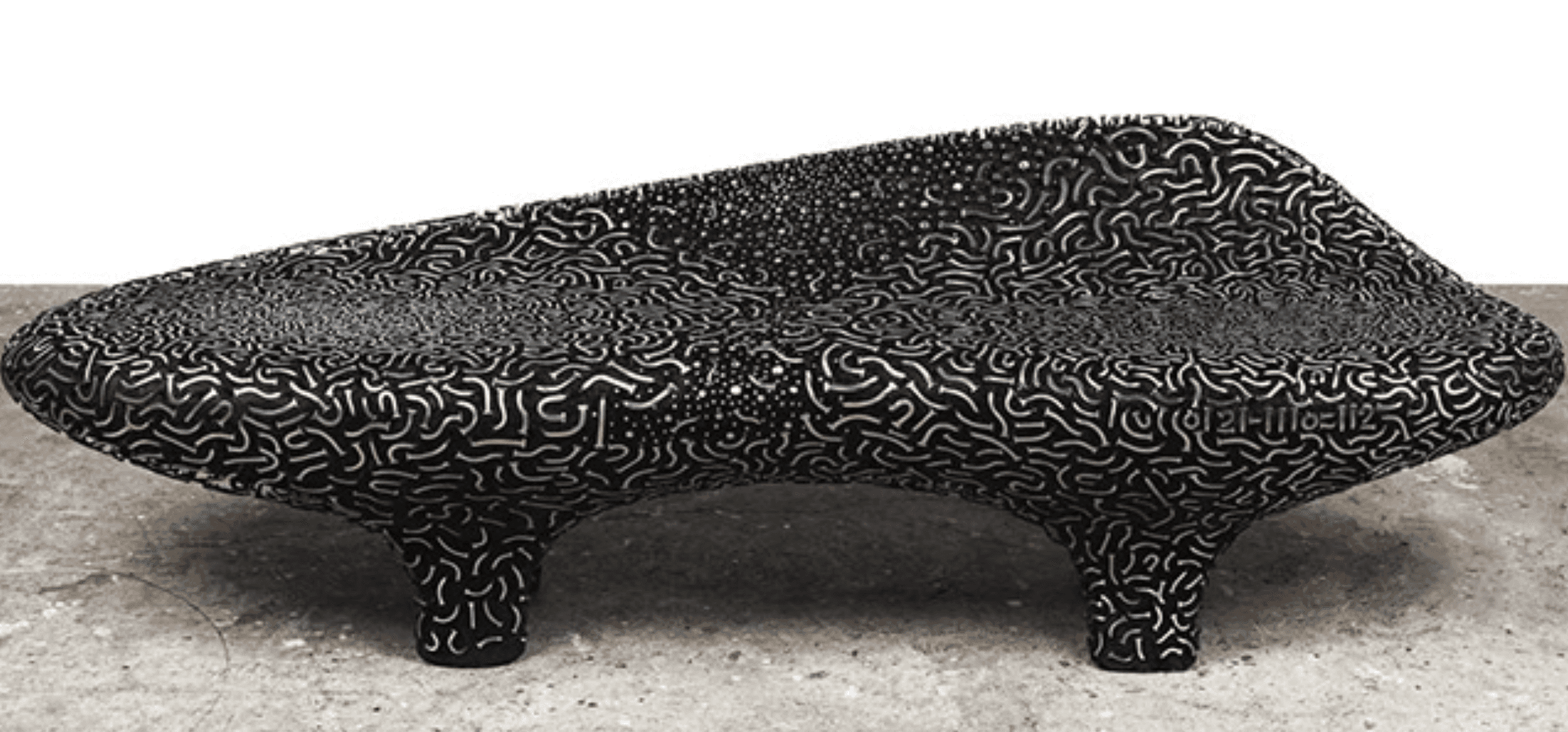 A highly sculptural, free-form sofa or lounge bench featuring an organic, undulating silhouette. The entire piece, including its two integrated, flared legs, is covered in a dense, repeating pattern of light-colored, calligraphic squiggles and dots on a dark, likely black, background. The backrest is integrated into the continuous, molded form, gently sloping upwards. Its appearance suggests a rigid, artistic construction rather than a traditional upholstered sofa. — 3D model