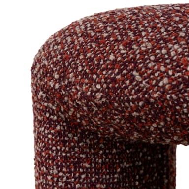 A U-shaped stool upholstered in a textured, multi-colored fabric. The stool has a rounded top and two cylindrical legs connected by a central arch, forming an open space in the middle. The upholstery features a mix of deep red, white, and light brown fibers, creating a speckled appearance. — 3D model