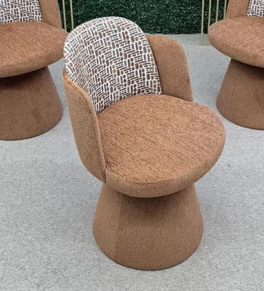A contemporary upholstered armless accent chair featuring a plush, rounded seat and backrest. The chair is entirely upholstered in a textured light brown/tan fabric, with the inner backrest showcasing a contrasting white and brown abstract geometric pattern. It rests on a solid, cylindrical pedestal base, suggesting swivel functionality. — 3D model
