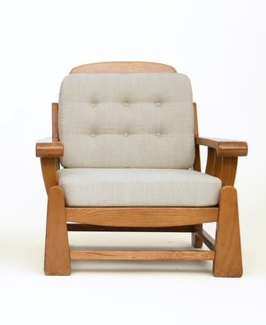 A sturdy, craftsman-style lounge chair featuring a solid oak wood frame and thick, upholstered cushions. The chair has broad, rounded arms, slatted side panels, and block legs. The back cushion is button-tufted. — 3D model