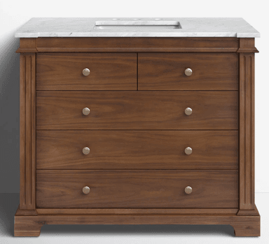 A traditional style bathroom vanity constructed from rich brown wood, featuring a white marble countertop with an integrated sink basin. The vanity has a rectangular form with fluted pilaster details on the side stiles and rests on a plinth base. It is equipped with multiple drawers of varying sizes, each fitted with round, satin brass-toned knobs. — 3D model
