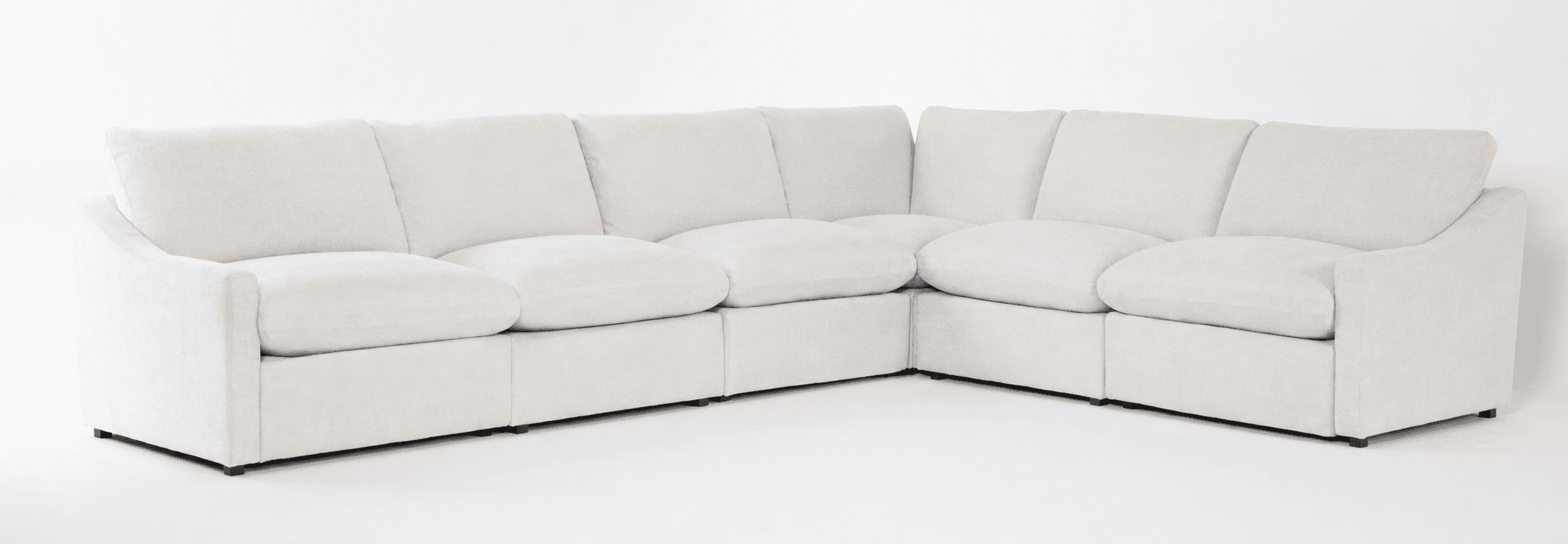 An off-white or cream-colored modular sectional sofa, configured in an L-shape. It features deep, plush seat cushions and backrests, giving it a soft and inviting appearance. The individual modules are upholstered in a light-colored fabric, likely linen or a similar texture. The design is contemporary with clean lines, subtly curved armrests, and low-profile dark feet that are minimally visible. — 3D model
