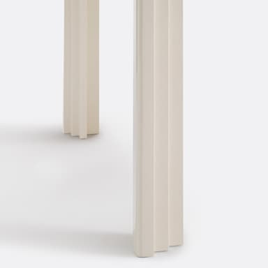 A close-up view of a table's surface and leg. The surface appears to be a high-gloss, off-white material, reflecting light. The leg has a distinctive carved design with layered, curved elements, reminiscent of a waterfall or architectural molding. The overall construction suggests a modern or contemporary style. — 3D model