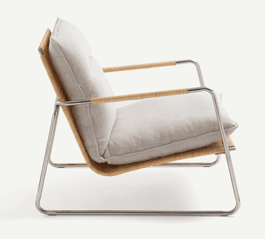 A low-profile modern lounge chair featuring a sleek, polished tubular steel frame. The seat and backrest are constructed from tightly woven natural cane, providing a textured, organic element. Thick, light-colored fabric cushions rest on the cane surfaces for comfort. The integrated armrests are part of the continuous steel frame, with a wrapped detail on the top sections. — 3D model
