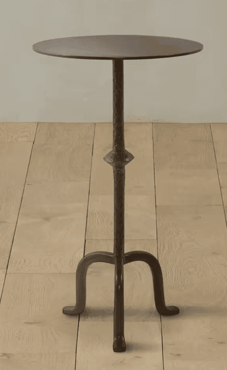 A tall, dark metal pedestal table featuring a round, flat top with a subtle hammered texture. The central column has a pronounced hammered finish and a decorative bulge midway down, transitioning into three elegantly curved legs that provide a stable, tripod base. The finish is a matte, dark bronze or antique iron. — 3D model