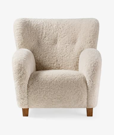 An inviting upholstered armchair featuring a plush cream-colored sheepskin or bouclé fabric, with a rounded silhouette, integrated armrests, and subtle wooden legs. — 3D model