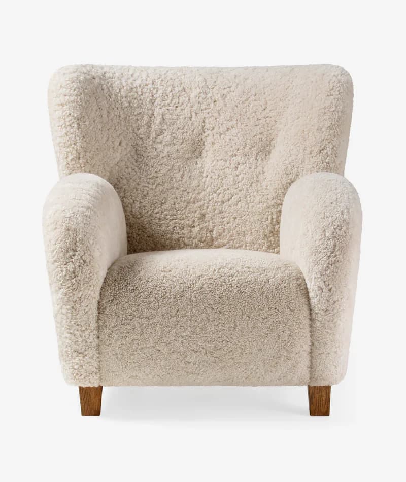 An inviting upholstered armchair featuring a plush cream-colored sheepskin or bouclé fabric, with a rounded silhouette, integrated armrests, and subtle wooden legs. — 3D model