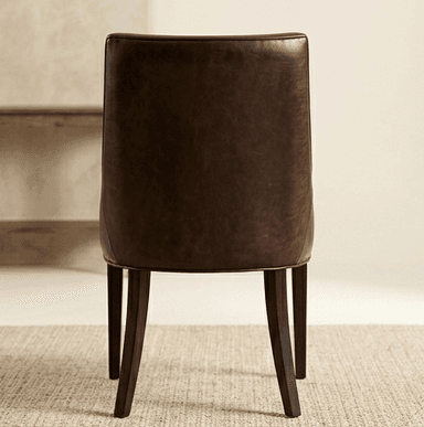 A dark brown dining chair viewed from the back. The chair features a curved, upholstered backrest and a seat base supported by four tapered wooden legs. The upholstery appears to be leather or a similar material with a matte finish. The legs are dark and slender, angled slightly outwards. — 3D model