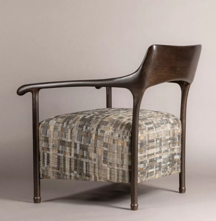 A modern armchair featuring a dark, sculptural wooden frame that forms the armrests, backrest, and legs. The armrests curve gracefully, extending from the backrest and supported by a leg structure. The seat is upholstered in a textured fabric with a multi-tonal geometric pattern in shades of beige, grey, and subtle orange. The chair presents a contemporary aesthetic with clean lines and organic shapes. — 3D model