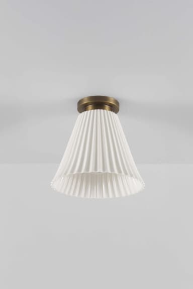 A white pleated bell-shaped light fixture mounted flush to a white ceiling. The fixture features a matte brass circular plate that attaches to the ceiling, from which the fluted, conical shade extends downwards. The light source within the shade is illuminated, casting a warm glow and highlighting the vertical pleats. — 3D model