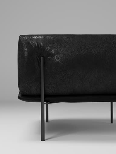 A contemporary armchair with a low profile, featuring a rounded, enveloping back and armrests. The upholstery has a textured appearance, suggesting leather or a high-quality fabric. It is supported by four slender, dark-colored legs that elevate the seat from the floor. — 3D model