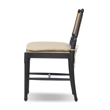 A contemporary dining chair featuring a solid black wooden frame, a natural woven rattan backrest, and a light beige fabric cushion positioned on a cane seat. The chair incorporates turned elements on its back posts and subtly tapered legs. — 3D model