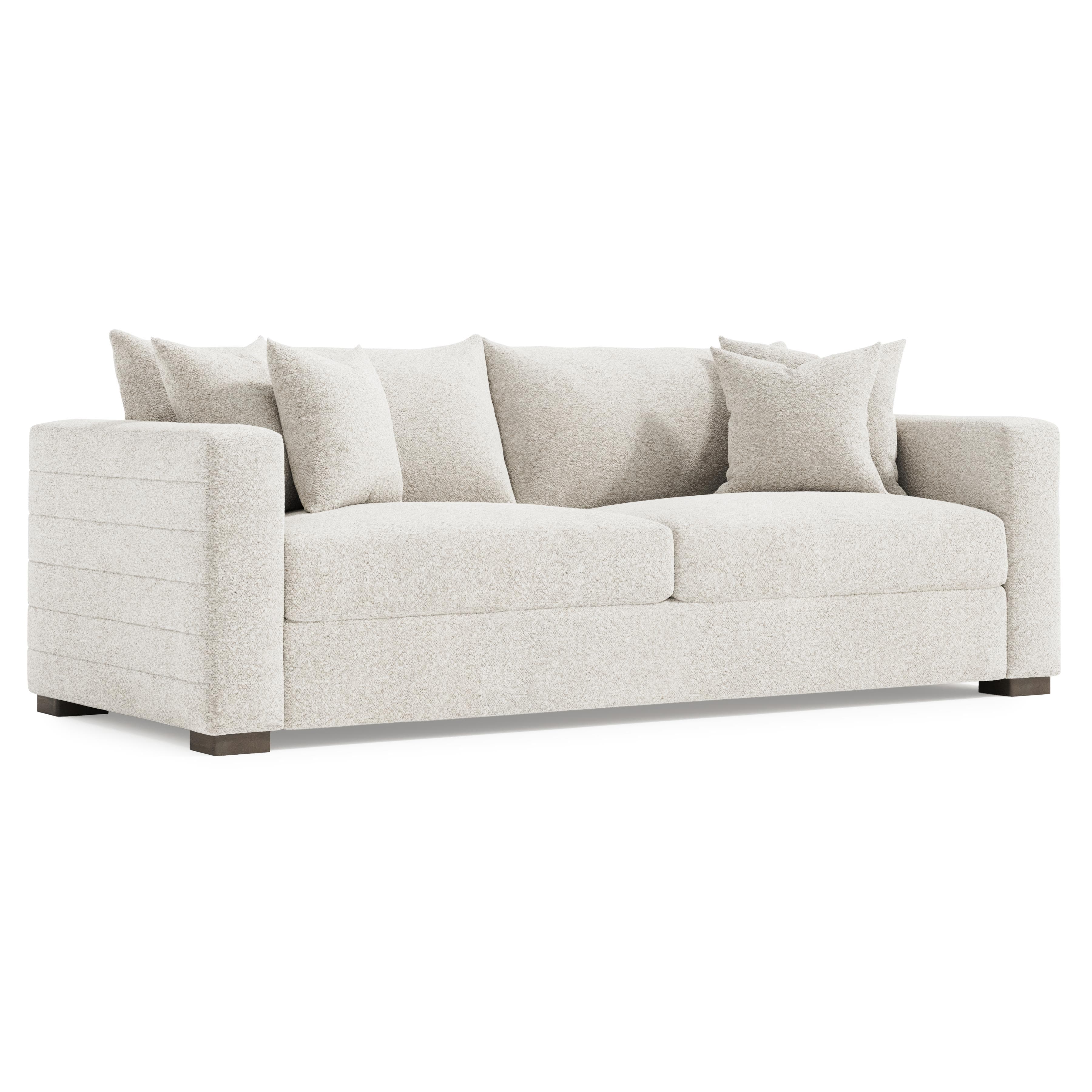 A modern, upholstered sofa with a textured, boucle-like fabric in a light neutral color. It features a low profile, clean lines, and is accented with horizontal channel detailing on the arms and side panels. The sofa includes three back cushions and two throw pillows, all with a similar textured fabric. It rests on dark, rectangular block feet. — 3D model