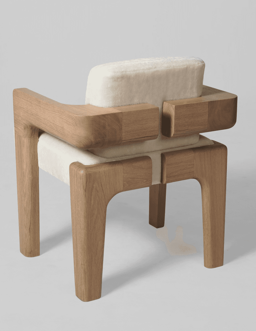 An armchair with a distinct contemporary design. The frame is constructed from light-colored wood with a visible grain, featuring robust legs and armrests. The seat and backrest are upholstered in a textured, off-white fabric that appears soft and plush. The design incorporates geometric shapes, with the wooden elements forming block-like structures that cradle the upholstered cushions. — 3D model