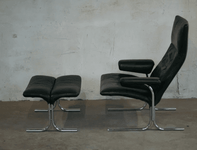 A black leather armchair with a matching ottoman. The chair features a high back and a curved, cantilevered chrome base. The ottoman also has a curved chrome base and is upholstered in matching black leather with a segmented cushion design. — 3D model