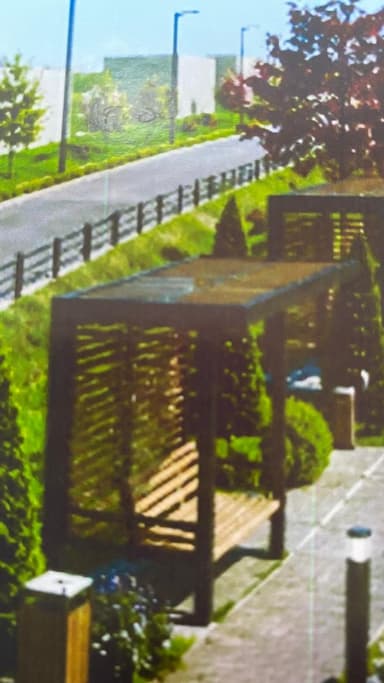 An isometric digital rendering of a modern outdoor pergola with an integrated slatted wooden bench. The structure features a dark brown timber frame supporting a lighter-toned slatted roof and a matching slatted bench. It is set on a paved area, flanked by green bushes and shrubbery. — 3D model