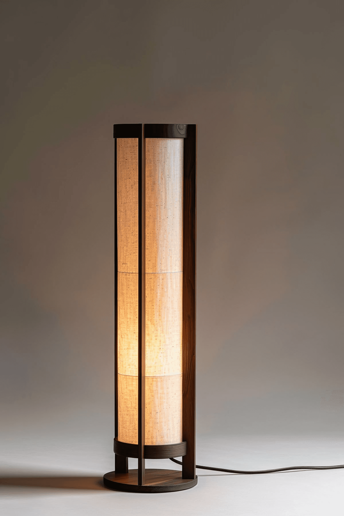 A modern floor lamp featuring a tall, rectangular column design. The lamp consists of a dark brown wooden frame that encases light-colored fabric panels, which diffuse the light. It stands on a matching circular wooden base and includes a visible power cord extending from the bottom. — 3D model