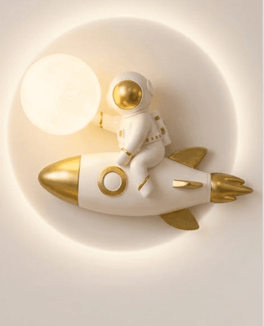 A whimsical wall-mounted lamp featuring a white and gold astronaut figure sitting atop a matching rocket, set against a circular, diffused light background. — 3D model
