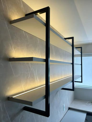 A contemporary four-tiered wall-mounted shelving unit featuring light gray shelves and a matte black metal frame. Each shelf has an integrated LED light strip on its underside, designed to illuminate the shelf below. — 3D model