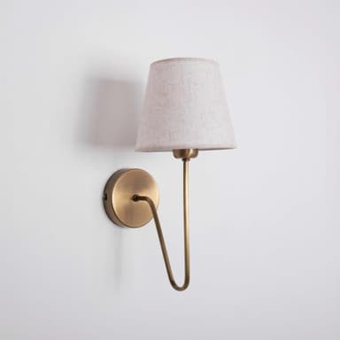 A wall-mounted lamp with a conical, cream-colored fabric shade and a brass-finished metal arm and base. The arm has a gentle curve and extends from a circular base plate mounted on the wall. The shade is open at the bottom and tapers upwards. — 3D model