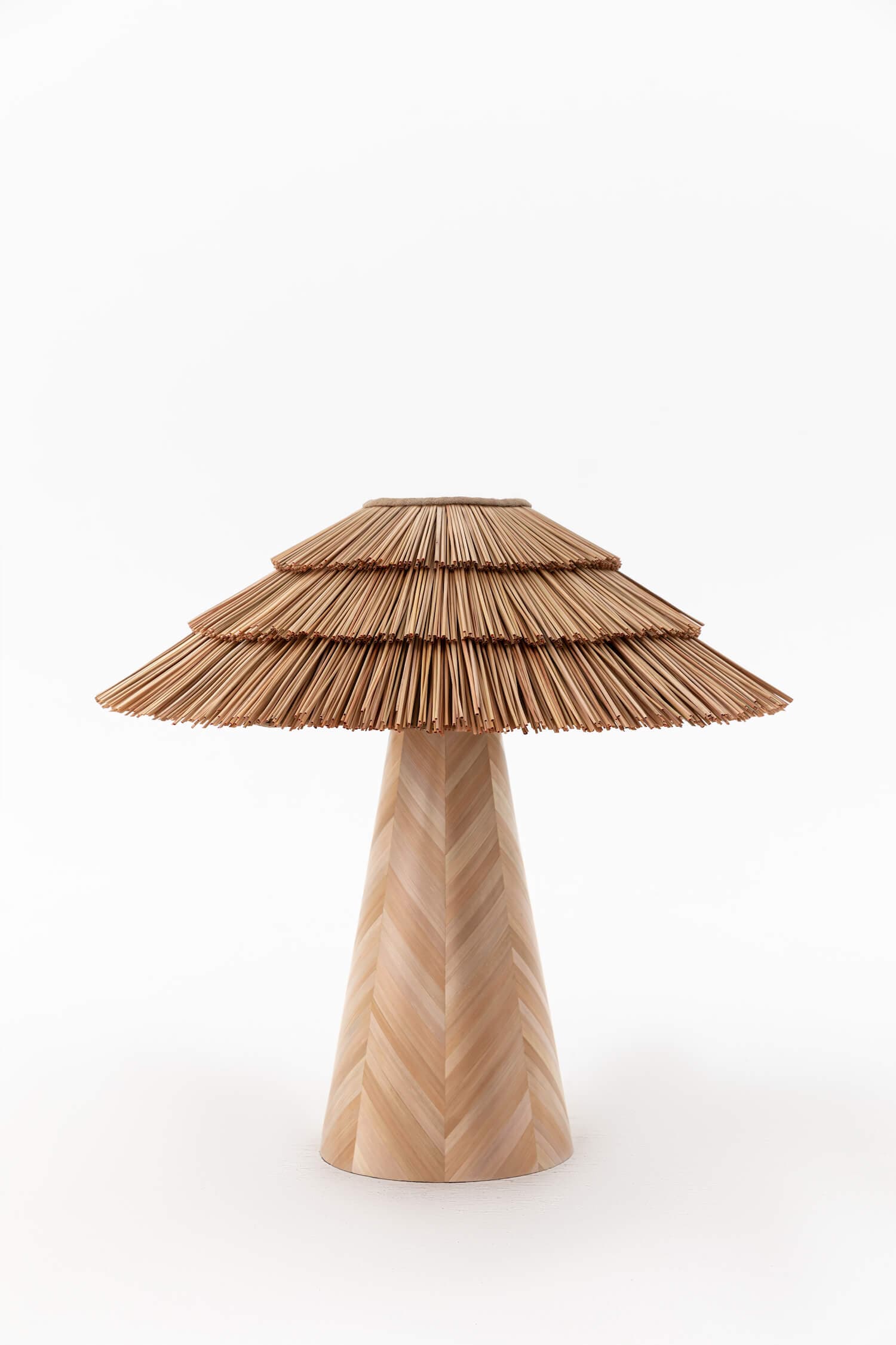 A table lamp with a tiered, pagoda-style shade made of natural straw or reeds. The base is conical, constructed from light-colored wood arranged in a chevron or herringbone pattern. — 3D model