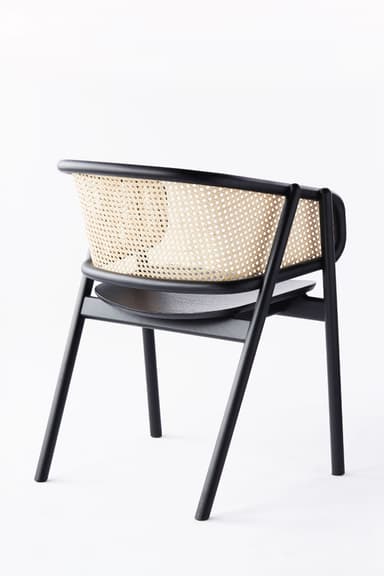 A modern armchair featuring a black finished solid wood frame, a natural cane woven backrest, and a light grey upholstered seat cushion. The chair has a sleek, minimalist design with integrated armrests that flow from the backrest. — 3D model