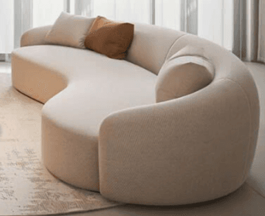 An S-shaped, curvilinear sofa upholstered in a light beige fabric, featuring soft, rounded edges and an integrated backrest/armrest design. It comes with two accent cushions, one light beige and one brown, complementing its neutral color palette. — 3D model