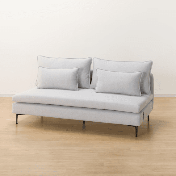 A contemporary armless chaise loveseat, upholstered in a light gray textured fabric. It features a low-profile design with a deep, elongated seat on the right side, resembling a chaise. The seating is supported by minimalist black metal legs, and the piece includes two large back cushions and two smaller rectangular throw pillows, all with subtle piped edges. — 3D model