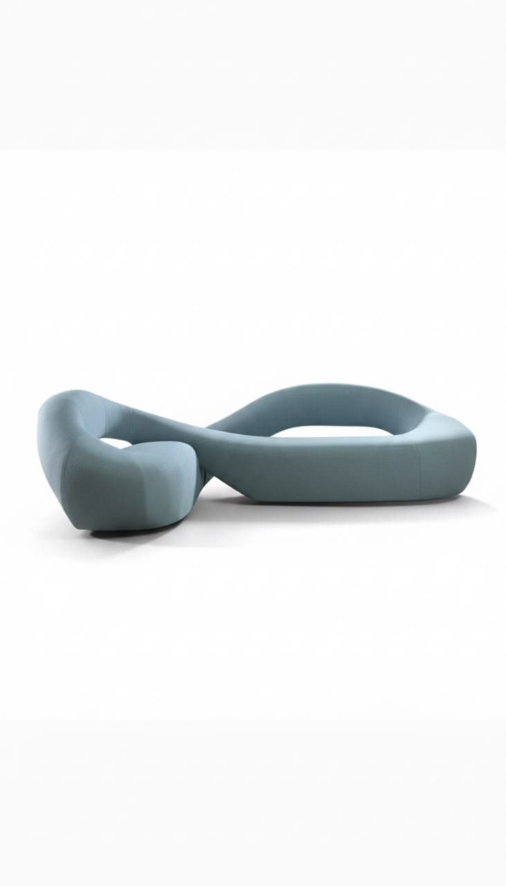 A sculptural, modern serpentine sofa upholstered in a light blue or teal fabric. The piece features a continuous, flowing form, resembling an abstract ribbon or an infinity symbol, with integrated seating areas. Its design is organic and avant-garde, resting directly on the floor with no visible legs, suggesting a low-profile silhouette. — 3D model