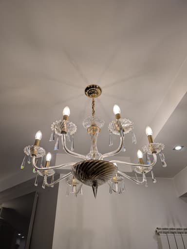 A multi-tiered chandelier with eight arms, featuring clear glass elements and crystal pendants. The central body has a twisted glass design, and the arms are curved, supporting candle-style light bulbs. The hardware appears to be gold-toned. — 3D model