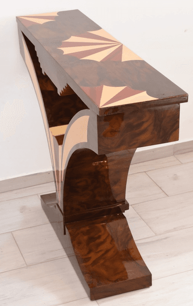 An elegant console table featuring a dark wood finish adorned with intricate marquetry. The rectangular tabletop displays a central sunburst pattern, flanked by geometric designs in contrasting lighter wood. The table's base consists of two large, sweeping curved supports that meet at a central point and transition into a sturdy, ornate plinth. These legs are also embellished with contrasting wood inlays that highlight their graceful, sculptural form. A single, small drawer with a simple pull is subtly integrated beneath the tabletop. — 3D model