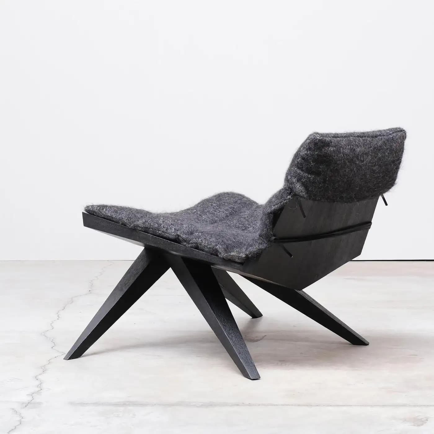 A low-profile, modern lounge chair featuring a dark, angular wooden frame and a thick, soft grey felted wool cushion. — 3D model