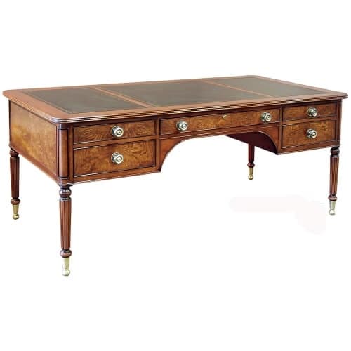 A traditional executive desk crafted from rich, reddish-brown wood, likely mahogany or a similar veneer, featuring a dark leather-inlaid top. The desk has a rectangular surface with rounded edges and is supported by four fluted, tapered legs that terminate in brass sabots or casters. The front apron includes multiple drawers: two stacked on each side and one central, wider drawer, all adorned with circular brass pulls. A kneehole design is present between the two side drawer banks. — 3D model