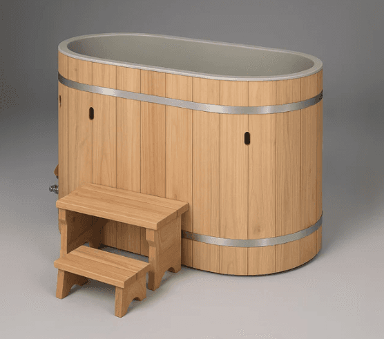 An oval-shaped bathtub with vertical wooden planks forming the exterior walls, reinforced by two horizontal metal bands. The interior lining appears to be a solid, light gray material. A small wooden step stool with two tiers is positioned in front of the bathtub. The bathtub has visible fittings on the side, suggesting it is functional for water supply and drainage. The overall aesthetic suggests a rustic or natural design. — 3D model