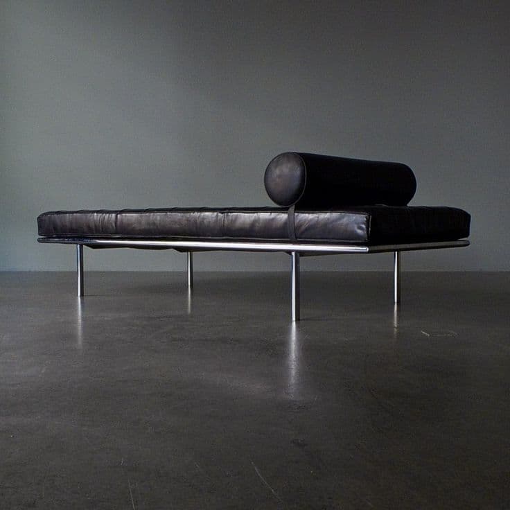 A tufted black leather daybed with a cylindrical bolster pillow. The daybed has a sleek, modern design with a polished chrome frame and thin, cylindrical legs. The upholstery features deep button tufting arranged in a diamond pattern across the main seating surface. — 3D model