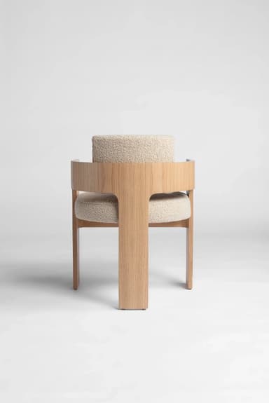 A modern accent chair featuring a distinctive T-shaped oak wood frame and integrated curved backrest/armrests, upholstered with cream bouclé fabric cushions. — 3D model