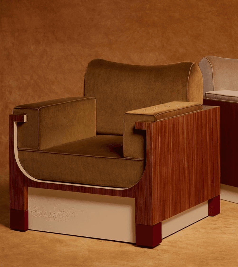 A modern upholstered armchair featuring a striking rectilinear wood frame with contrasting velvet cushions. The chair has a boxy profile with wide, flat armrests and a thick seat cushion, all covered in a warm olive-brown velvet. The frame is constructed from a dark, rich wood with visible grain, forming the sides and back. A light-colored panel forms the lower front and sides, supported by four reddish-brown block feet. A distinctive curved wooden element connects the armrest to the chair's back. — 3D model
