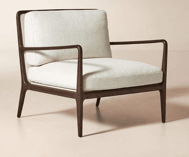 A contemporary armchair featuring a dark wood frame with a warm finish. The frame has a streamlined design with gently curved armrests that extend from the back. The chair is upholstered in a textured, off-white fabric on the seat, back cushion, and armrest pads. The overall design is minimalist and elegant, suitable for modern interiors. — 3D model