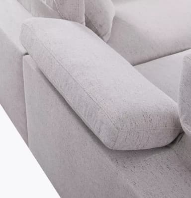 A section of a light gray, upholstered sofa is visible against a white background. The sofa features a modular design with distinct seat and backrest cushions. One armrest and part of a side cushion are also visible. The upholstery has a textured appearance with a subtle flecked pattern. — 3D model