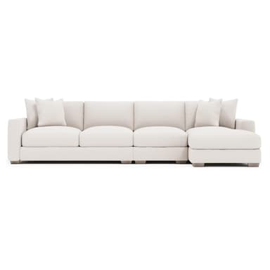 A contemporary sectional sofa, upholstered in a light-colored, textured fabric. It features a chaise lounge on the right side and comes with multiple throw pillows. The sofa has clean lines, plush cushions, and low-profile wooden legs. — 3D model