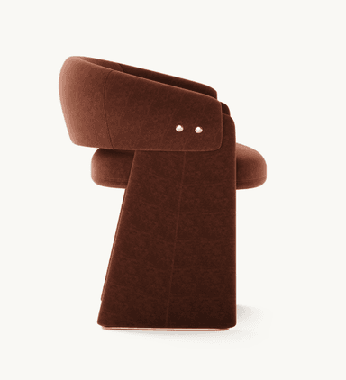 A contemporary armchair featuring a sculptural, curved silhouette upholstered in rich reddish-brown velvet. It has wide, solid, U-shaped legs and brass stud detailing on the back. — 3D model