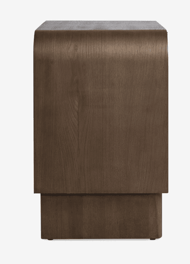 A contemporary nightstand featuring a dark-stained wooden frame with gently rounded top edges. It includes a single drawer with a woven cane front and a small brass knob, positioned above an open lower storage shelf. The base is a solid, plinth-like structure with subtle, short legs. — 3D model