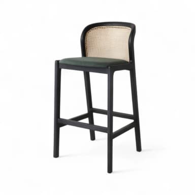 A modern bar stool featuring a solid black wooden frame, a natural cane woven backrest, and a dark green upholstered seat. The stool has four legs and integrated footrests for stability and comfort. The backrest is gently curved, offering ergonomic support. — 3D model