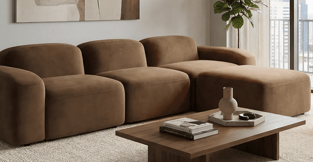A contemporary modular sectional sofa upholstered in a brown fabric, featuring multiple individual sections and an accompanying ottoman. The design emphasizes rounded edges and a low profile. — 3D model