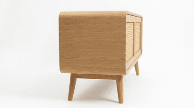 A contemporary, low-profile storage cabinet crafted from light-colored oak wood, featuring smoothly rounded corners on the top, sides, and front panel. It stands on four splayed and tapered legs, presenting a minimalist design with a single large front panel that likely functions as a door for enclosed storage. — 3D model