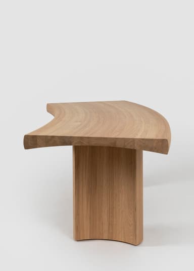 A modern curved bench crafted from light-toned solid oak wood. The design features a gently bowed top surface supported by two thick, substantial legs that are seamlessly integrated and follow the curvature of the top, creating a cohesive, sculptural form. The wood displays a natural grain, emphasizing its organic aesthetic. — 3D model